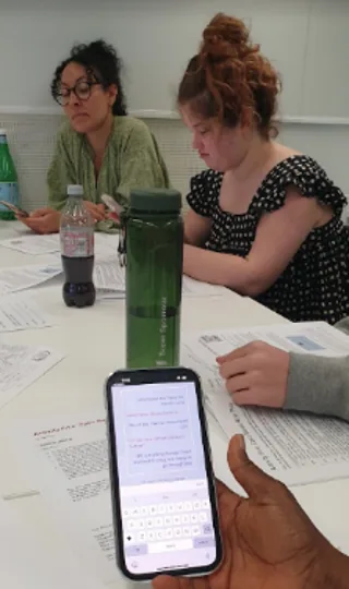 Students using a phone-based AI roleplay activity around a table